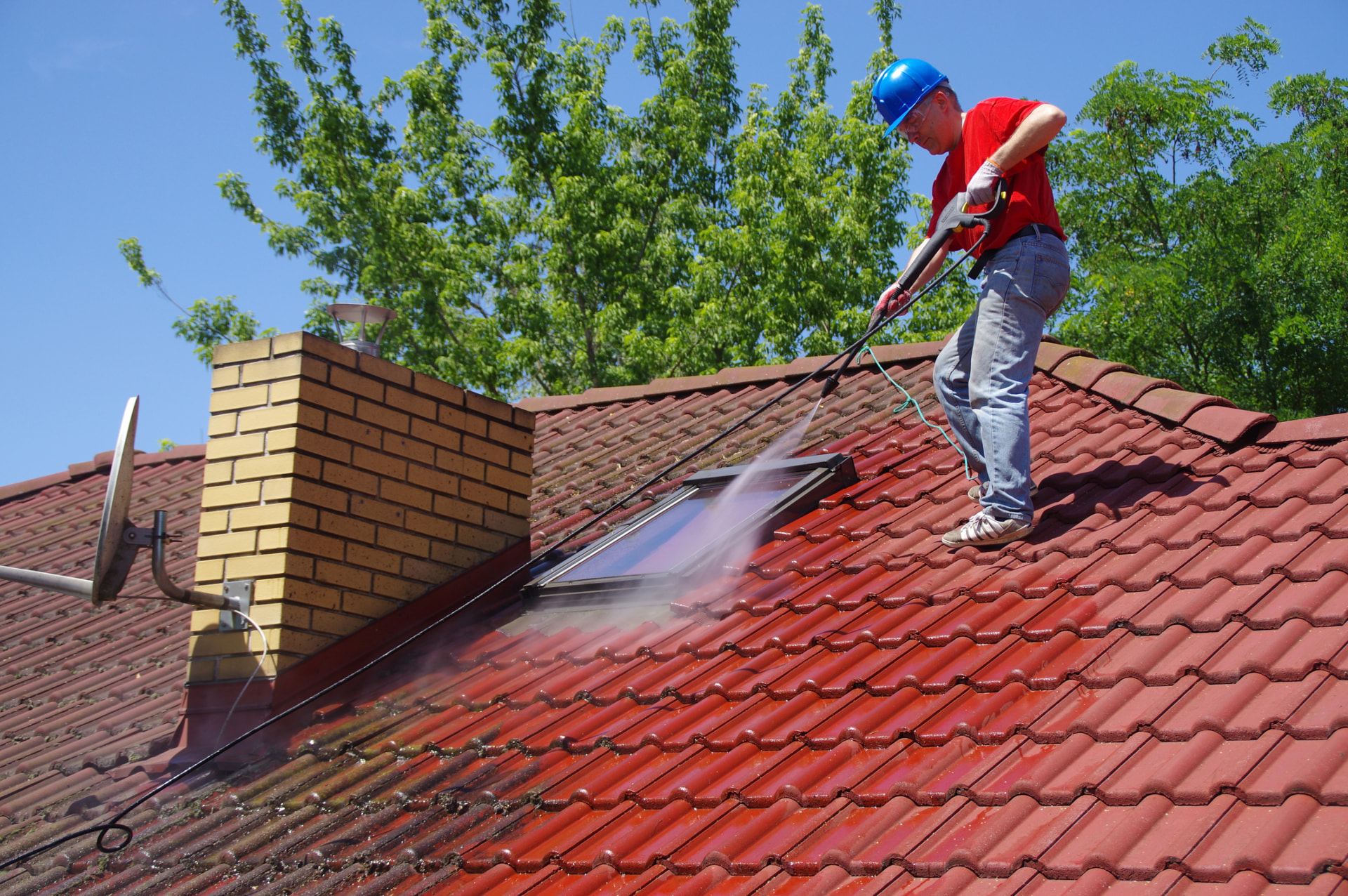 Technician cleaning a tile roof with a low-pressure wash on a sunny day