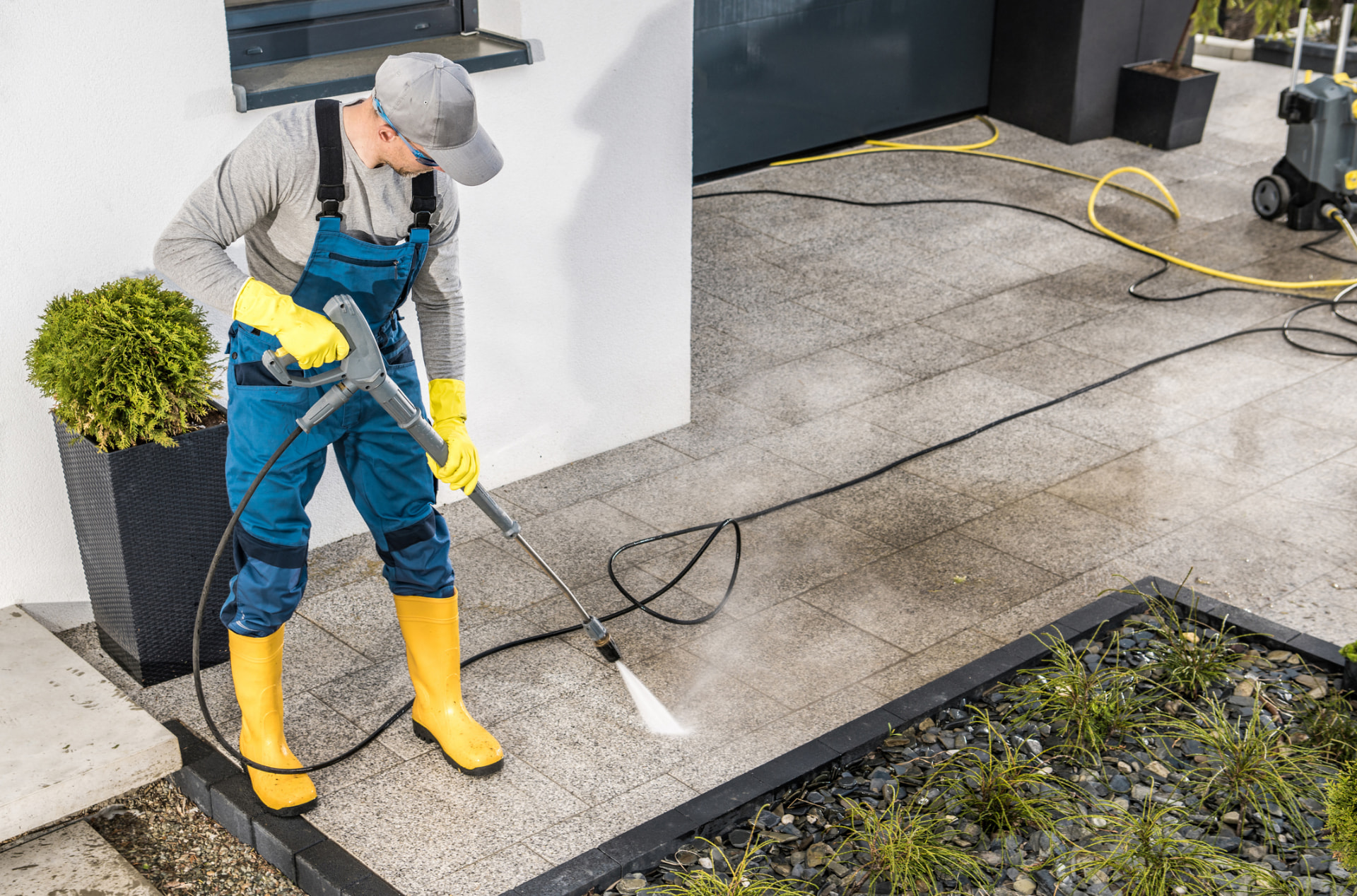 AllClear technician pressure washing a paver driveway and walkway outside a modern home