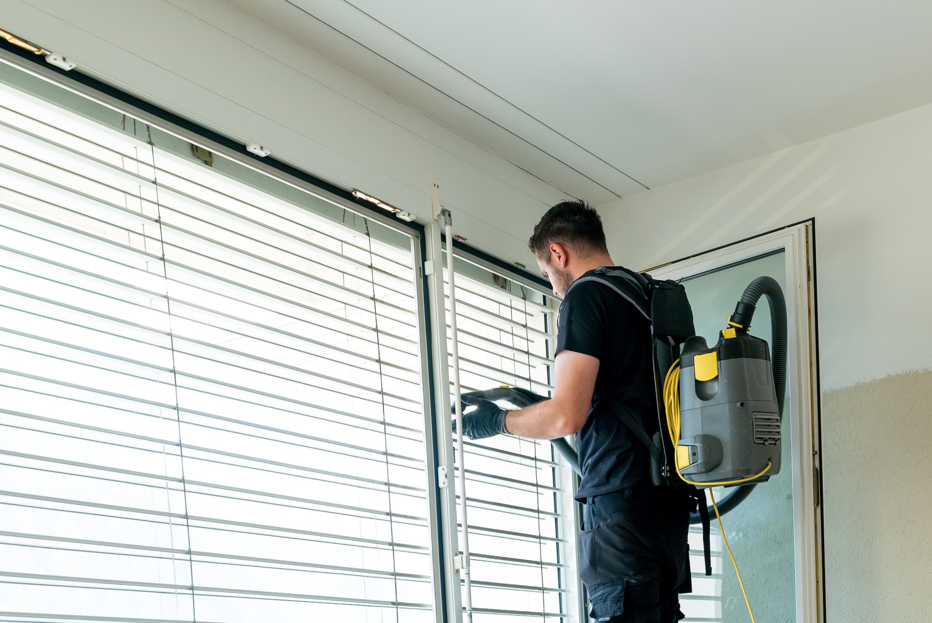 Technician vacuuming window blinds and tracks during an interior window cleaning