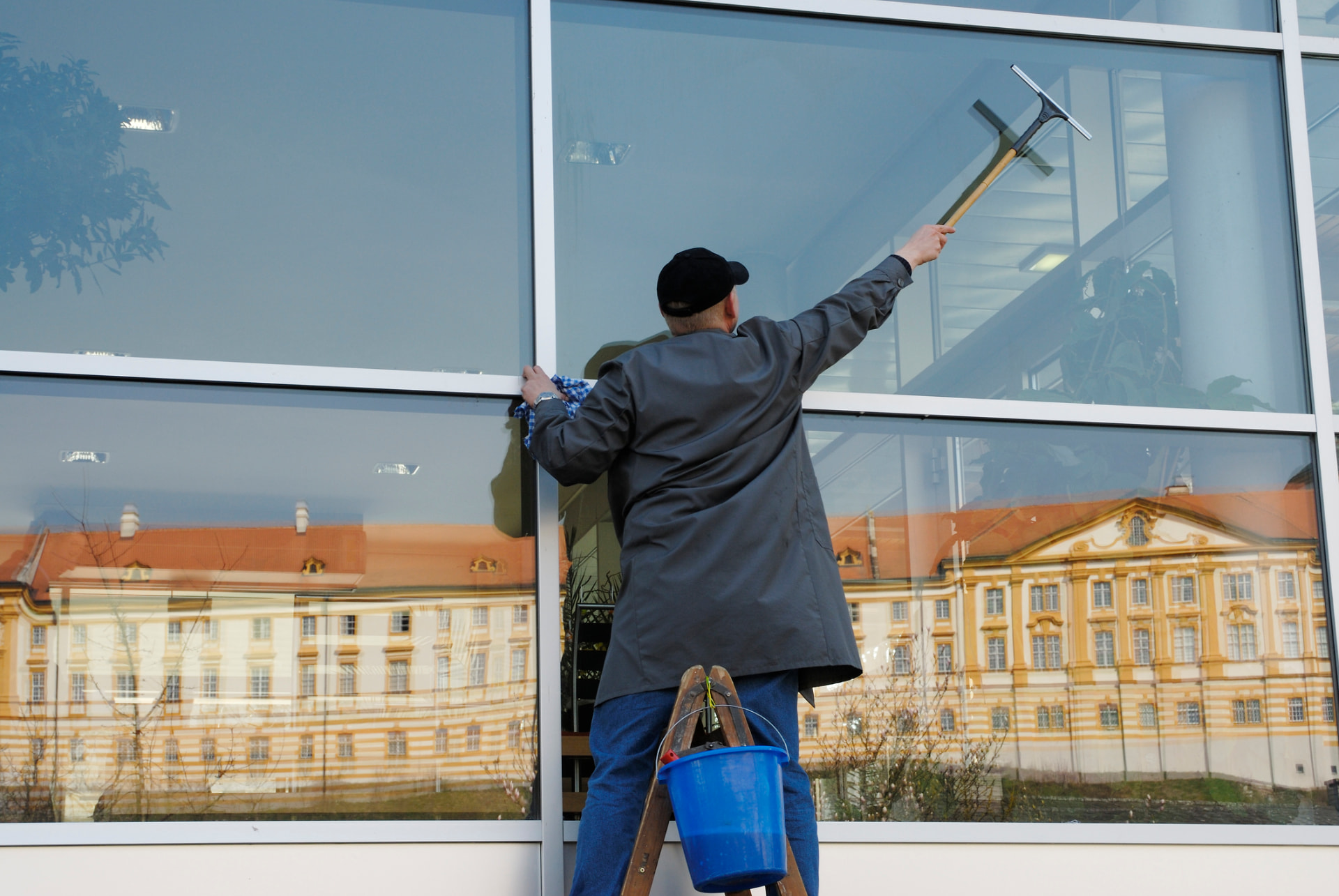Window cleaner on a ladder squeegeeing large commercial glass panels