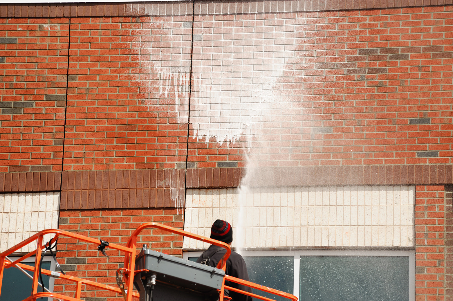 Soft washing a brick commercial building exterior from a lift in Northeast Ohio